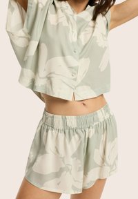 Jasnozielony dwuczęściowy zestaw w kwiatowy wzór, składający się z koszuli z krótkim rękawem, posiadającej guziki, oraz spodenek z elastycznym paskiem. Miękka tkanina, luźny krój.