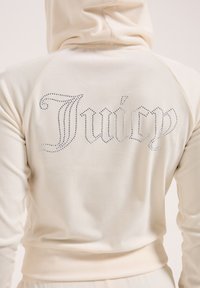 Felpa color crema realizzata in un morbido tessuto, con cappuccio e un grande logo "Juicy" decorato con strass sul retro.