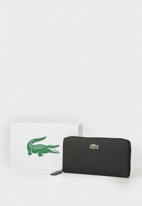 Čierna peňaženka na zips s textúrovaným povrchom, so zeleným a červeným logom krokodíla Lacoste. Dodáva sa v bielej krabičke s logom.