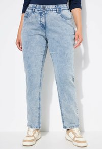 Vaqueros de mezclilla azul claro con un ajuste relajado, piernas rectas y bolsillos frontales. Combinados con zapatillas ligeras con acentos en beige.