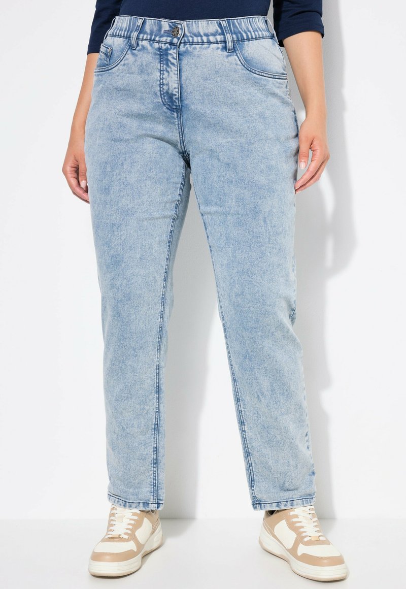 Vaqueros de mezclilla azul claro con un ajuste relajado, piernas rectas y bolsillos frontales. Combinados con zapatillas ligeras con acentos en beige.