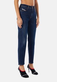 Mörkblå denimjeans med rak benmodell, fem fickor och en lätt blekning framtill. Bärs med svarta och röda högklackade skor.