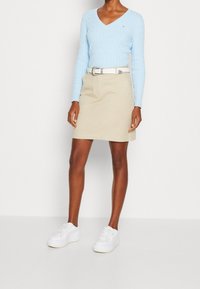 Ljusblå, kabelstickad v-ringad tröja, beige kjol med bälte och vita sneakers. Outfiten har en figurnära design med en slät textur.