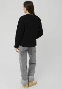 Pull en polaire noir avec une surface texturée, coupe décontractée et manches longues, associé à un jean gris taille haute et des chaussures à plateforme beiges.
