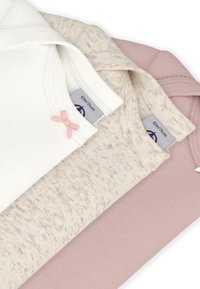 Three children's tops in white, beige with a speckled pattern, and light pink. Features include a pink bow accent and soft cotton fabric.