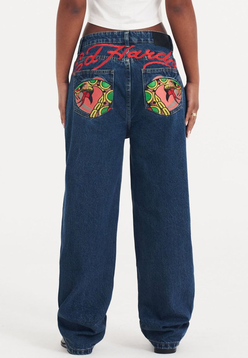 Jeans de mezclilla de pierna ancha con un lavado azul oscuro, que cuentan con bordados coloridos de serpiente y cadena en los bolsillos traseros y el logo rojo "Ed Hardy".