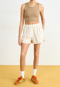 Top court côtelé beige associé à un short crème avec des rayures verticales jaunes, et des baskets orange avec des accents verts. Chaussettes blanches visibles.