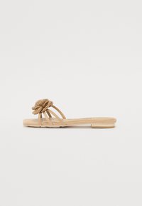 Flat sandal with a beige faux-leather base, three slender straps, and a textured braided flower accent on the upper. Minimalist design.