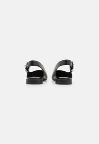 Schwarze Leder-Sandalen mit einem Rückenschenkel, ovalen Perforationen im oberen Bereich und einem strukturierten Fußbett. Niedrige, flache Gummisohle mit Schnallendetail.