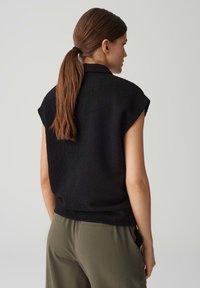 Top corto a maniche corte nero texturizzato con vestibilità rilassata, visto da dietro, abbinato a pantaloni verde oliva.