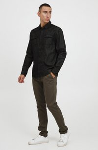 Črna srajca s kratkimi rokavi, z dvema žepoma na prsih, teksturirana tkanina. V kompletu z olivno zelenimi hlačami in belimi športnimi copati, ima slim fit kroj.