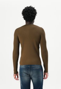 Braunes, geripptes Langarmoberteil mit rundem Halsausschnitt, kombiniert mit medium-wash Denim-Jeans mit Gesäßtaschen und dezentem roten Logo.