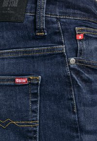 Tamnoplave traperice, stražnji džep i petlja za remen s žutim šavovima i crvenim oznakama koje sadrže bijele zvjezdice i natpis "Big Star".