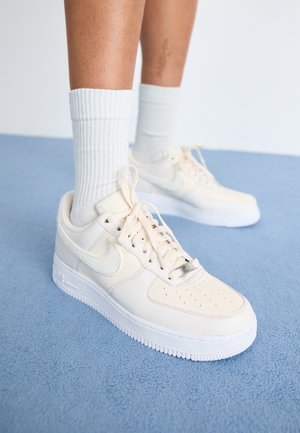 Personne portant des baskets Nike blanches montantes et des chaussettes blanches côtelées debout sur un tapis bleu clair.
