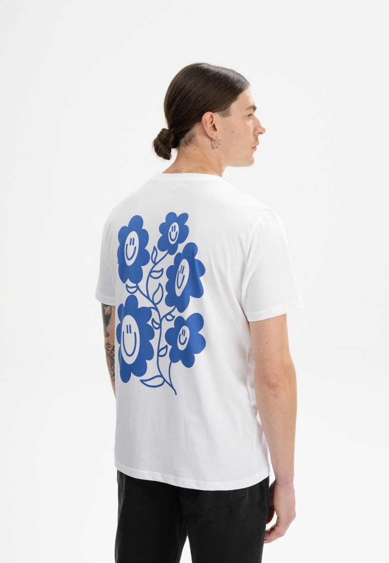 Witte katoenen t-shirt met een blauw bloemenontwerp met lachende gezichten. Korte mouwen en een relaxte pasvorm. Eenvoudige, strakke lijnen.