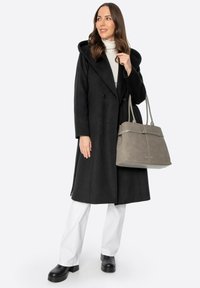 Černý vlněný kabát s velkou kapucí a dvoubarevnými knoflíky, v kombinaci se šedou semišovou kabelkou. Modelka má na sobě bílé kalhoty a černé platformové boty.