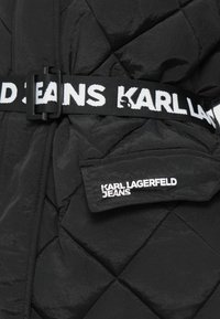 Giacca nera trapuntata con una larga cintura nera con il testo bianco "KARL LAGERFELD JEANS" e un piccolo logo a patch sul davanti. Materiale testurizzato.
