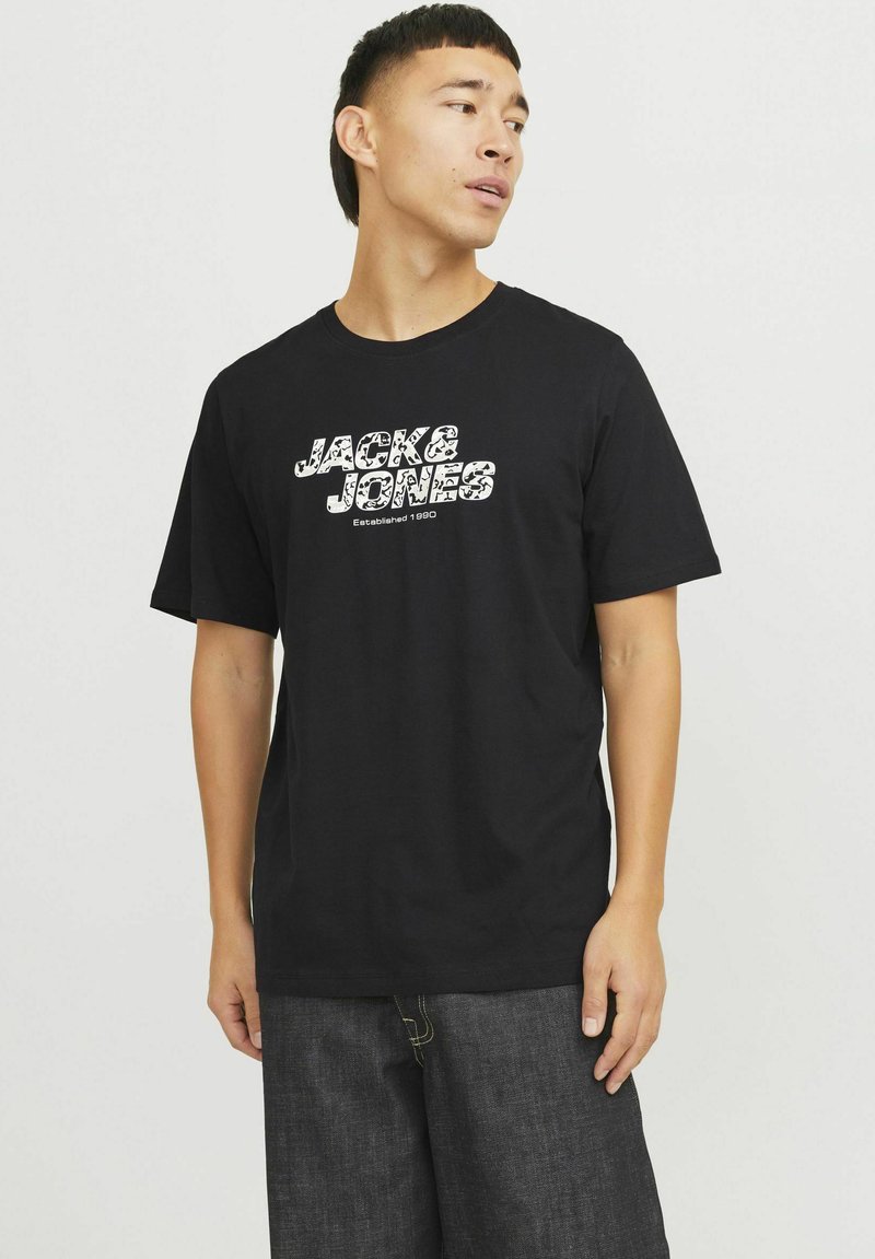 Sort bomulds t-shirt med en hvid grafisk trykning af "JACK & JONES" og "Etableret 1990" i en afslappet blokskrift. Korte ærmer.