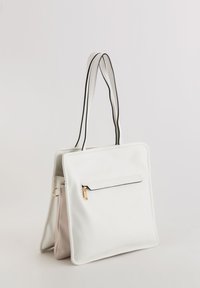 Hvid læder tote bag med en struktureret form, kontrasterende sorte kanter, en frontlomme med lynlås og dobbelte stropper. Blødt beige interiør synligt.