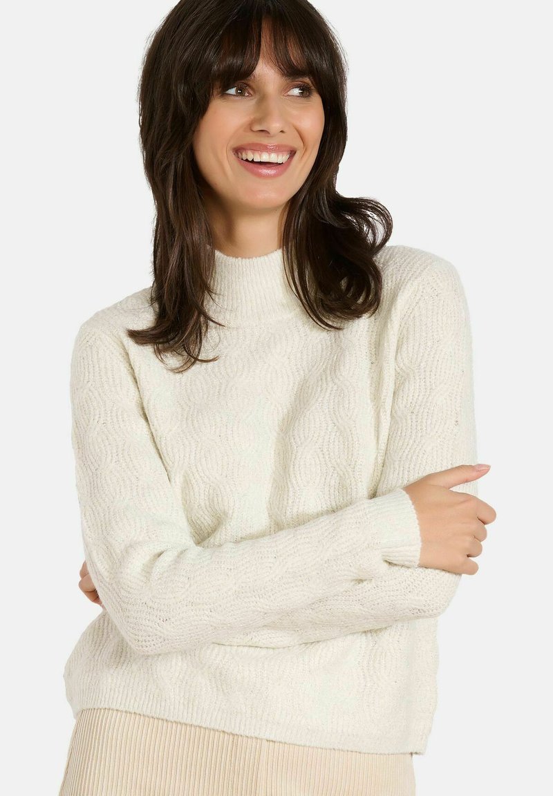 Cremfarbener, strukturiert gestrickter Pullover mit hohem Kragen, langen Ärmeln und einer leicht verkürzten Passform. Besitzt ein Wellenmuster über das gesamte Kleidungsstück.