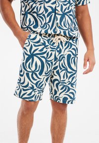 Heren shorts in crème met een blauw bloemenpatroon, voorzien van een elastische tailleband met een trekkoord. Gemaakt van lichtgewicht stof.
