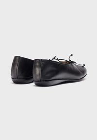 Bailarinas de cuero negro con una textura suave, punta redondeada y lazos decorativos en la parte delantera. Diseño elegante con acentos minimalistas.