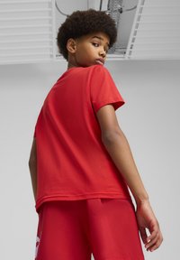 Camiseta de algodón roja con mangas cortas, textura suave y un ligero escote redondo. Llevada con pantalones cortos rojos a juego, vista desde atrás.