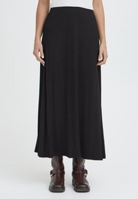 Črna maxi krila iz mehkega blaga z širokim, gladkim pasom. Ima tekoč dizajn, ki se razteza do gležnjev, v kombinaciji z rjavimi škornji.
