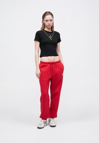Czarny skrócony t-shirt i czerwone spodnie dresowe z elastycznym pasem; białe sneakersy z czarnymi akcentami. Prosty design, casualowy wygląd.