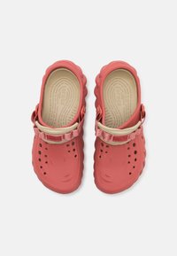 Coral red clogs with cut-out holes, adjustable strap, textured sole, and cushioned interior. Made from lightweight synthetic material.
