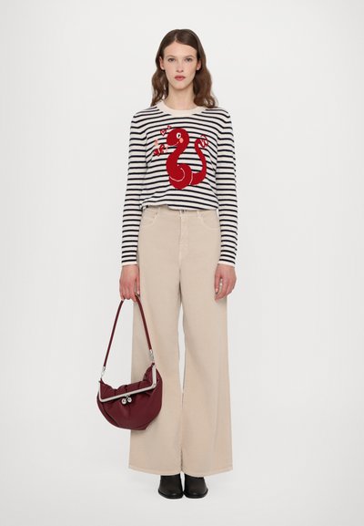 Striped sweater with a red snake design, paired with beige wide-leg pants. Model holds a maroon handbag with a silver accent. Black shoes.