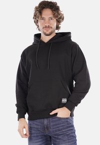 Felpa nera con cappuccio, tasca frontale, lacci e etichetta. Presenta una texture morbida e un design classico da indossare sopra, adatta per un look casual.