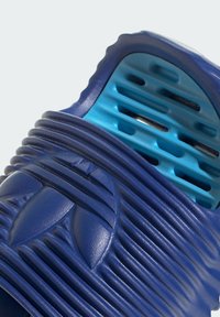 Blå gummiflips med räfflad textur, distinkt logodetalj och öppen design med ventilationsöppningar i en kontrasterande blå nyans.