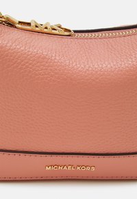 Neceser de cosméticos de cuero rosa con un acabado texturizado, materiales en dorado y detalle del logo "Michael Kors" en relieve en la parte inferior.