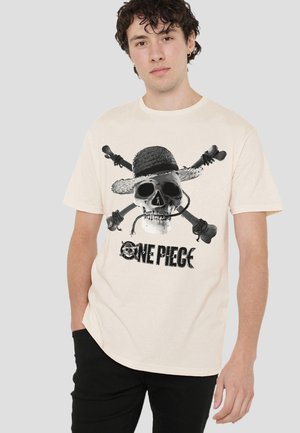 Young man wearing beige t-shirt with black skull and crossbones wearing a straw hat and "One Piece" text, standing against a light background.