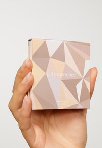 Kompaktowy bronzer w opakowaniu z geometrycznym wzorem, z delikatnymi neutralnymi odcieniami i błyszczącym wykończeniem. Tekst na przodzie: "LH cosmetics Infinity bronzer Luminous."