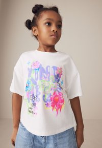 Hvid kortærmet t-shirt med farverige blomster- og sommerfuglgrafik samt tekst, parret med lyseblå denimshorts.