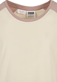 Kremfarget skjorte med lysebrune raglanermer, rund hals og synlig merke som viser Urban Classics-merket og pleieanvisning.