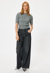 Grijze gebreide trui met korte mouwen en een textuurpatroon; hoge taille donkere denim wijde pijpen broek en metallic puntige schoenen.