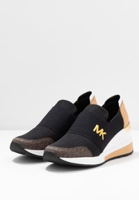 Baskets noires à enfiler avec une tige en maille, des accents en cuir, un logo doré, un talon compensé et un embout texturé marron. Semelle blanche et beige.