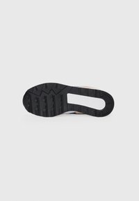 Sneaker outsole with rugged black rubber, featuring deep treads and a white midsection. Subtle beige accents near the heel area.