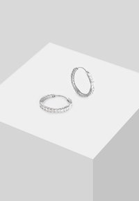 Orecchini a cerchio in argento con una fila di cristalli trasparenti incastonati lungo il bordo anteriore. Il design è liscio e circolare con una chiusura a cerniera.
