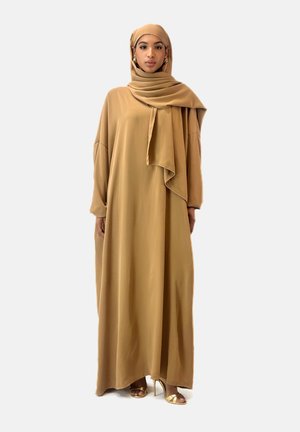 Robe longue beige en tissu lisse avec une coupe ample, des épaules tombantes et un hijab assorti. Comprend des accents dorés minimalistes sur les chaussures.