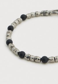 Βραχιόλι με μαύρες και ασημί χάντρες που διαθέτει μεταλλικές χάντρες με διαφορετικές υφές και λείες μαύρες σφαίρες, παρουσιάζοντας έναν απλό, κυκλικό σχεδιασμό.