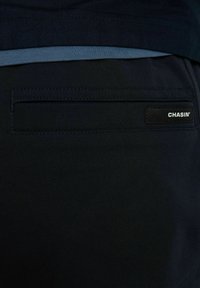 Crne tajice od rastezljivog materijala s plavim unutarnjim pojasom, s stražnjim džepom i malom oznakom brenda s natpisom "CHASIN'".