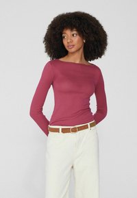 Langärmliges, geripptes Oberteil in tiefrosa, kombiniert mit cremefarbenen Hosen und einem braunen Gürtel. Hat einen weiten Ausschnitt und eine figurnahe Passform.