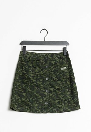Zielona spódnica dżinsowa w kamuflażu z przednimi guzikami i dwiema bocznymi kieszeniami, charakteryzująca się prostym krojem i fakturowanym materiałem, zawieszona na czarnym wieszaku.
