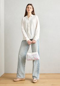 Biała prążkowana koszula na guziki, jasnoniebieskie szerokie spodnie dżinsowe, beżowe baleriny, torebka w kwiatowy wzór z łańcuszkiem, drewniana podłoga w tle.