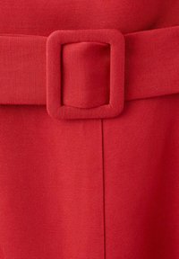 Gros plan d'une ceinture en tissu rouge avec une boucle rectangulaire assortie recouverte de tissu sur un vêtement rouge.