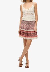 Top de ganchillo con escote en V en color blanco roto, combinado con una falda fluida de estampado floral con toques en rosa, púrpura y negro. Sandalias de tacón marrones.